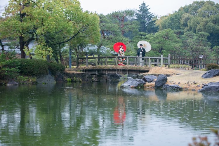 池にかかる橋で番傘をさしながら撮影する新郎新婦