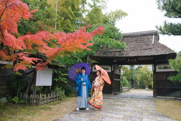 緑と赤の木々の下で和傘をさす新郎新婦