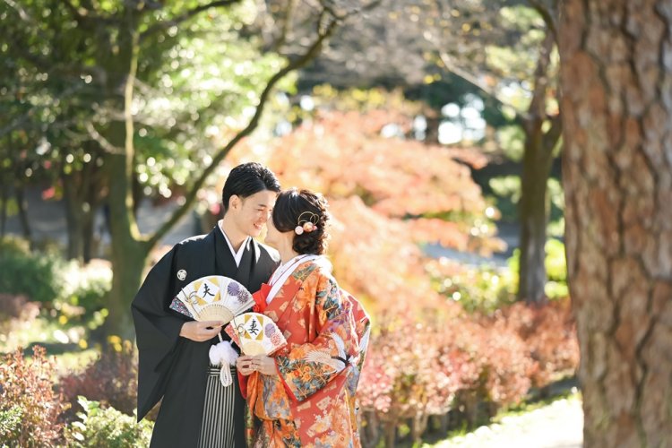 公園内の紅葉バックに扇子を手におでこを合わせる新郎新婦