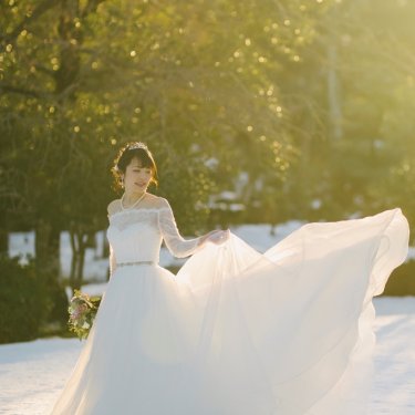 光の射す雪の積もった庭園でドレスをなびかせる新婦