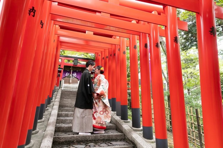 赤い鳥居の下で向かいあう新郎新婦