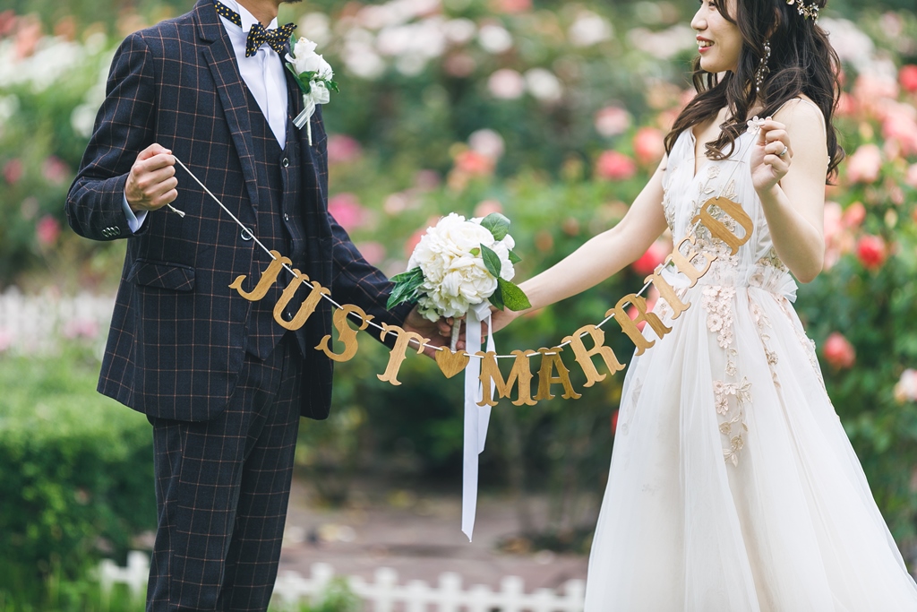 花咲く公園でガーランドとブーケを持つ新郎新婦