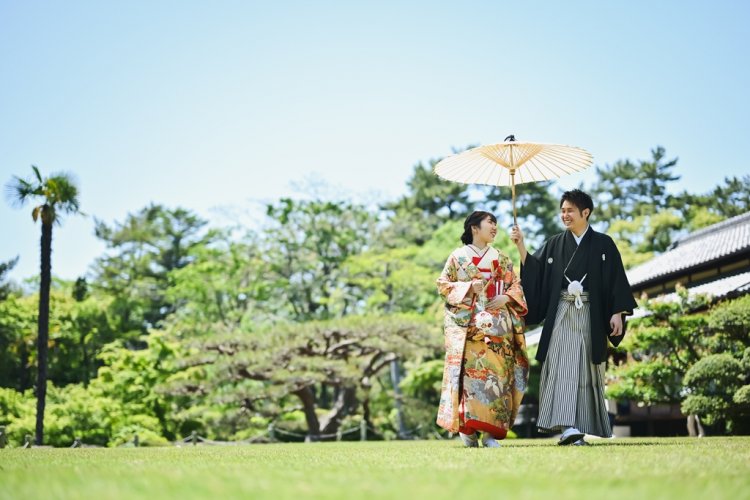 緑の庭園で一本の和傘に仲良く入って微笑み合う新郎新婦