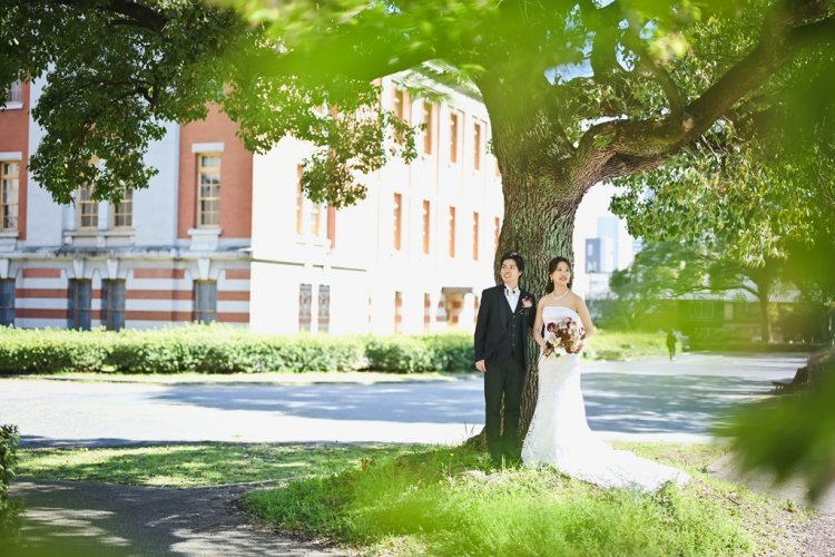 レンガ調の外観バックにした緑の公園で撮影